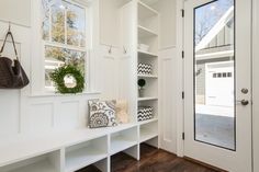 a white entryway with wooden floors and large mirror on the wall, next to a bench in front of an open door