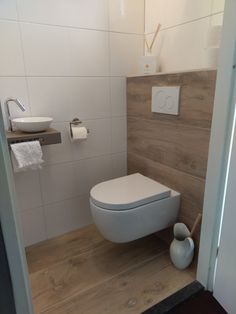 a white toilet sitting inside of a bathroom next to a wooden floor and wall mounted faucet