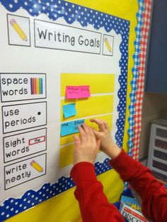 a person writing on a bulletin board with sticky notes and pencils attached to it