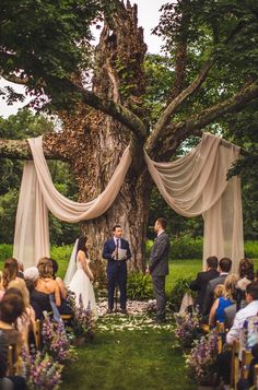 a couple getting married in front of an outdoor wedding ceremony with drapes draped over the trees