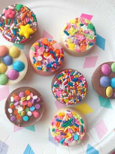 six decorated cupcakes on a plate with sprinkles