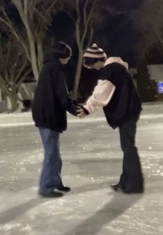 two people are standing in the snow holding each other's hands and looking at something