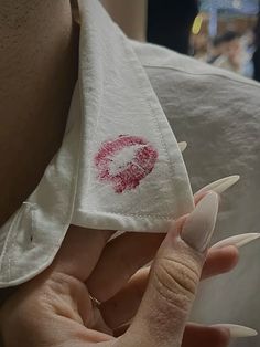 a person with white nails holding up a red lipstick print on a napkin over their left shoulder