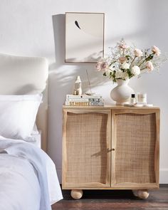 a bedroom with a bed, nightstand and flowers on top of the dresser next to it