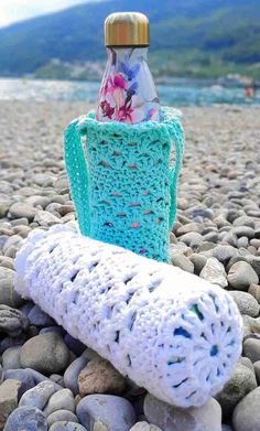 a crocheted bottle holder sitting on top of some rocks