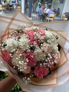 a bouquet of pink and white flowers is held by someone's hand in front of a restaurant