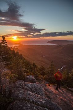 a man standing on top of a mountain looking at the sun setting in the distance