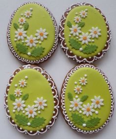 four decorated cookies with white daisies and green leaves on the top one has a letter e