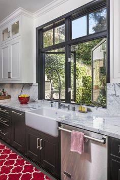 a kitchen with black cabinets and white marble counter tops is pictured in this image, there are red rugs on the floor next to the sink