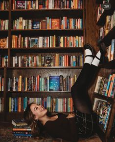 a woman laying on the floor in front of a bookshelf full of books