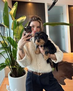 a woman taking a selfie with her dog and camera in front of a potted plant