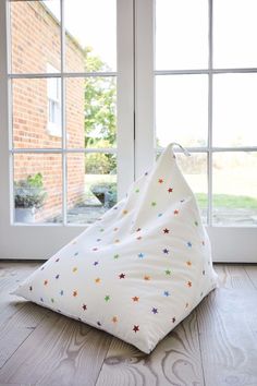 a white bean bag sitting on top of a wooden floor next to two large windows