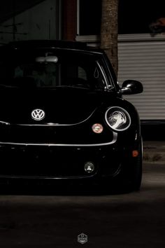 the front end of a black car parked in a parking lot at night with its lights on