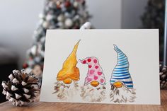 a card with three gnomes on it next to a pine cone