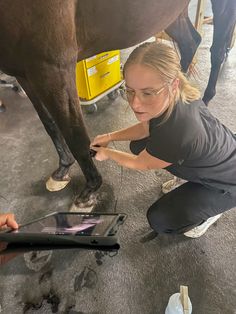 a woman kneeling down next to a horse on top of a floor with an ipad