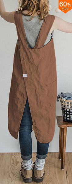 a woman standing in front of a wooden table wearing a brown apron over her shoulder