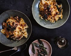 two plates filled with pasta and sauce on top of a black tablecloth next to silverware