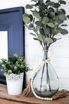 a vase filled with green leaves on top of a wooden table next to a potted plant