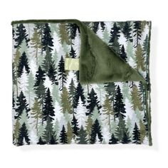 a green and white blanket with trees printed on the front, folded in two different colors