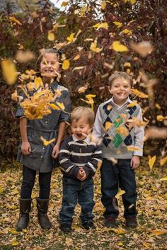 three children standing in front of some leaves