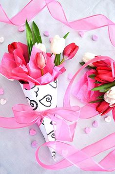 two pink and white flowers are in a vase with ribbon on the table next to it