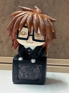 a ceramic figurine of a boy with glasses and hair sitting on a black box