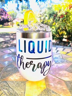 a drink glass with liquid therapy written on it sitting on a tiled surface in front of some trees