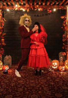 a man and woman dressed up in costumes standing next to each other with pumpkins around them