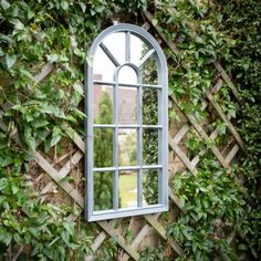 a mirror hanging on the side of a wall covered in green plants and ivys