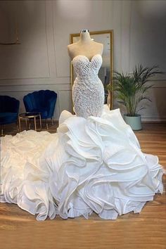 a white wedding dress on display in a room with blue chairs and a gold framed mirror