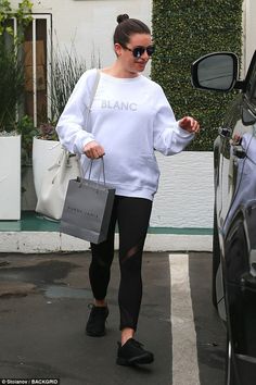 a woman in white sweatshirt and black leggings holding shopping bags while walking towards her car