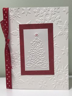 a white card with a red ribbon around it and a christmas tree on the front