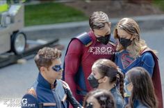 a group of people standing around each other wearing masks on their faces and looking at something in front of them