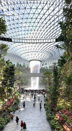 an indoor garden with lots of plants and people walking around the area, surrounded by glass roofing