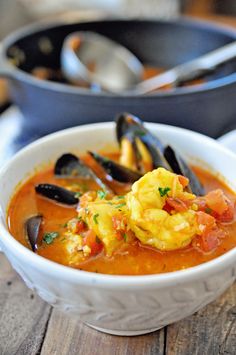 a white bowl filled with soup and mussels on top of a wooden table