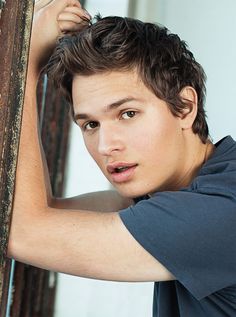 a young man leaning against a wooden pole with his hand on the top of it