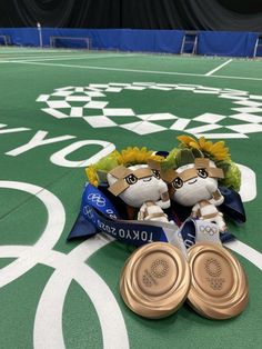 two gold medals sitting on top of a green field covered in white and blue ribbons