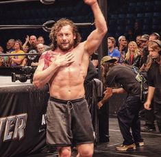 a man with no shirt standing in front of a wrestling ring holding his arm up