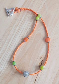 This necklace is made with orange seed beads, orange glass beads, green glass beads, metallic spacer beads, and a gray ribbed bead in the middle. Toggle clasp. Measures 20 inches long end to end. Adjustable Orange Beaded Necklaces With Tiny Beads, Adjustable Orange Beaded Necklace With Tiny Beads, Adjustable Orange Single Strand Beaded Necklace, Orange Necklaces With Spacer Beads For The Beach, Bohemian Orange Single Strand Beads, Orange Necklace With Spacer Beads For Beach, Adjustable Orange Beaded Necklace With Faceted Beads, Orange Beach Necklace With Spacer Beads, Adjustable Orange Necklaces With Colorful Beads