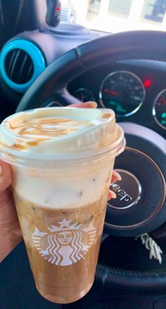 a person holding up a cup of coffee in their hand and steering wheel behind them