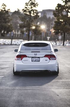 the back end of a white car parked in a parking lot next to some trees