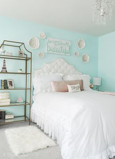 a white bed sitting under a chandelier next to a book shelf filled with books