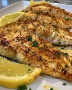 two pieces of fish on a plate with lemon wedges