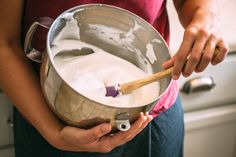 a woman holding a metal pan filled with white liquid and a wooden spoon in it