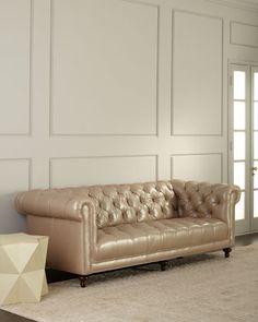 a tan leather couch sitting on top of a carpeted floor next to a white wall