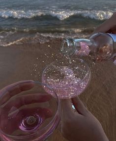 two people are toasting with wine glasses on the sand near the water's edge