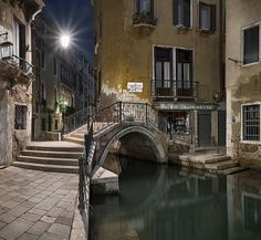 a bridge over a small canal in an old city at night with the lights on