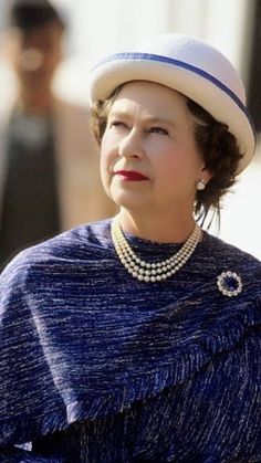 an older woman in a blue dress and hat with pearls on her neck, looking off to the side