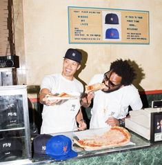 two young men are eating pizza at a restaurant counter with hats on their head and one is wearing a baseball cap