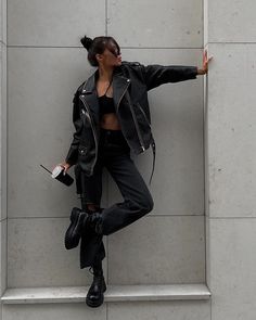 a woman leaning against a wall with her arms stretched out in the air and wearing all black